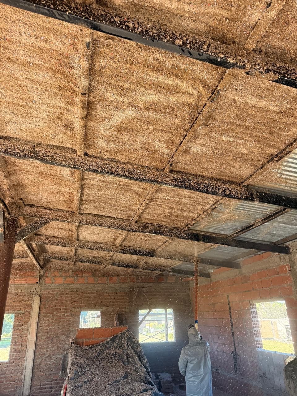 Aplicación de celulosa proyectada en techo, operario trabajando